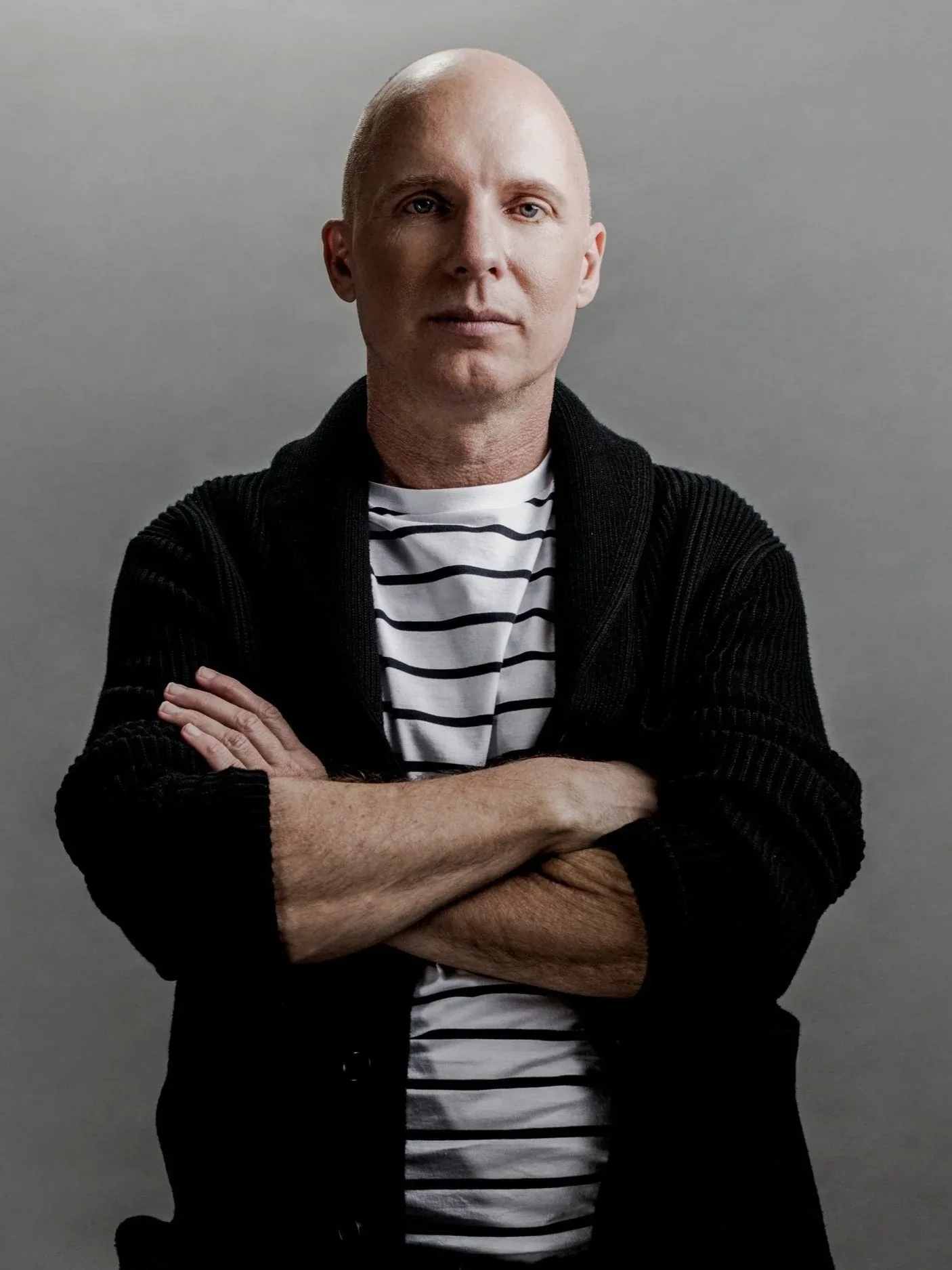 Composer Stephen Tackett with crossed arms in a black cardigan against a grey studio backdrop